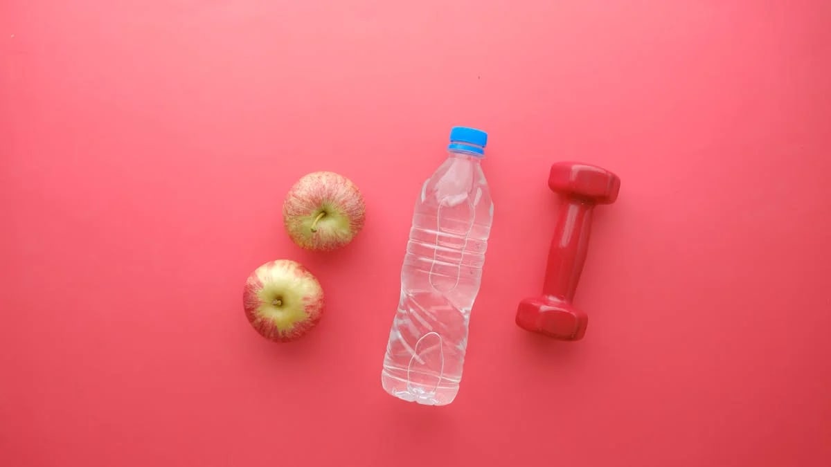 Top view of water bottle, apples, and dumbbell on bright red background. Perfect for fitness and wellness themes.